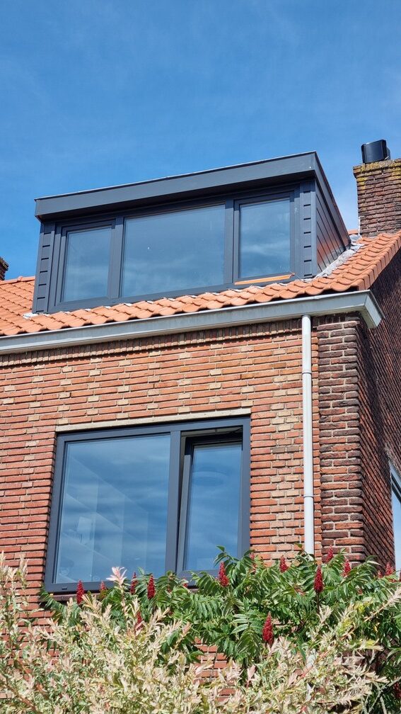 Dakkapel met donkere kozijnen aan een bakstenen woning door Select Kozijnen
