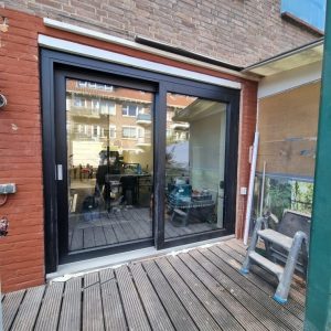 Schuifpui met donkere kozijnen aan een bakstenen woning door Select Kozijnen